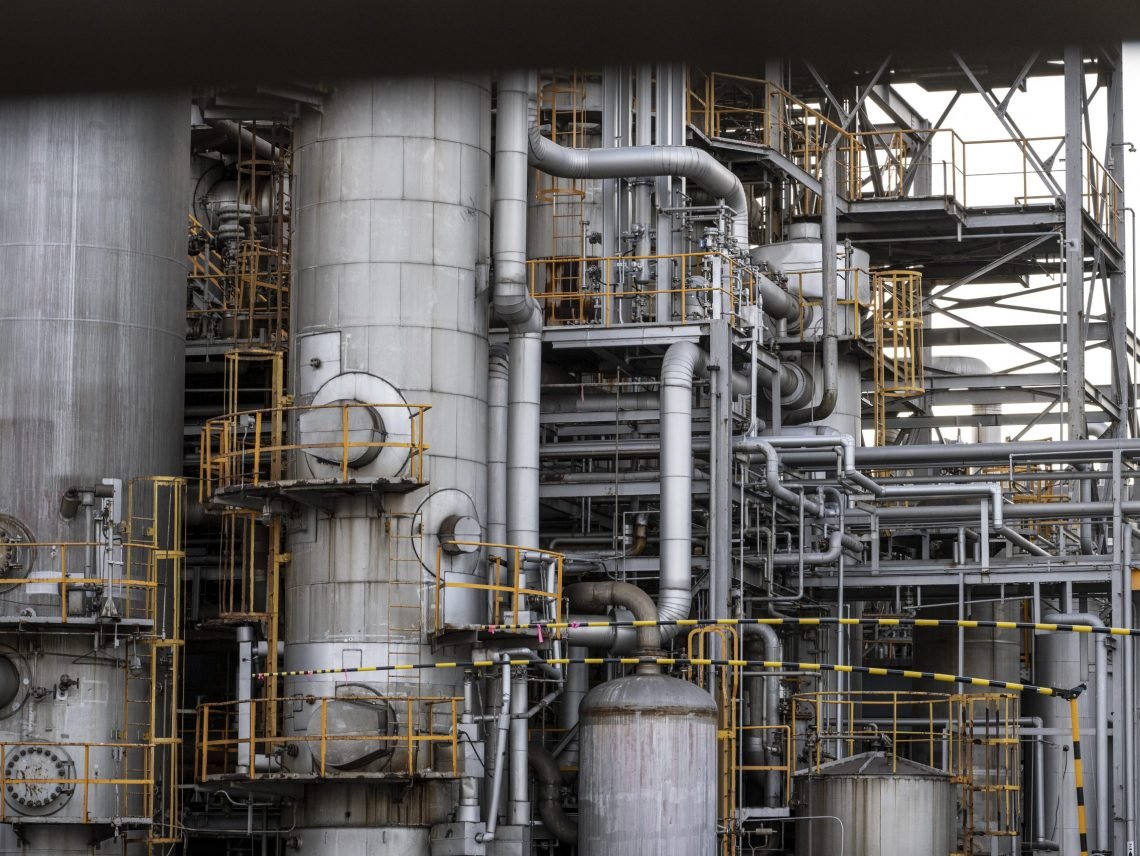 Complex industrial refinery structure with pressure vessels, metal piping, valves, and platforms used in chemical processing.