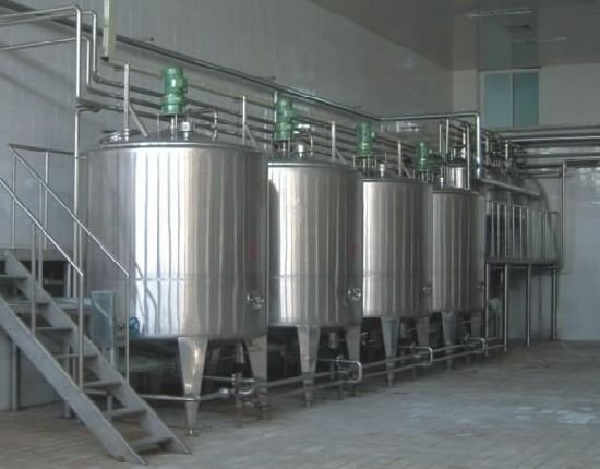 A row of stainless steel tanks sitting inside of a building.