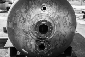 A close-up of a metallic pressure vessel with visible openings and pipes, displaying wear marks.