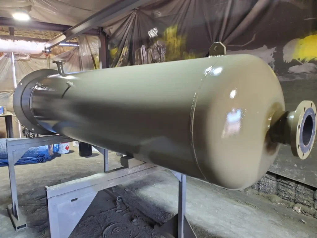 Beige cylindrical industrial pressure vessel tank resting on support frames in a manufacturing facility