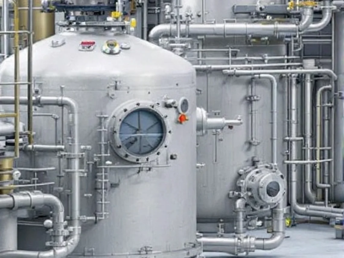 Stainless steel pressure vessel with gauges and piping in an industrial facility.