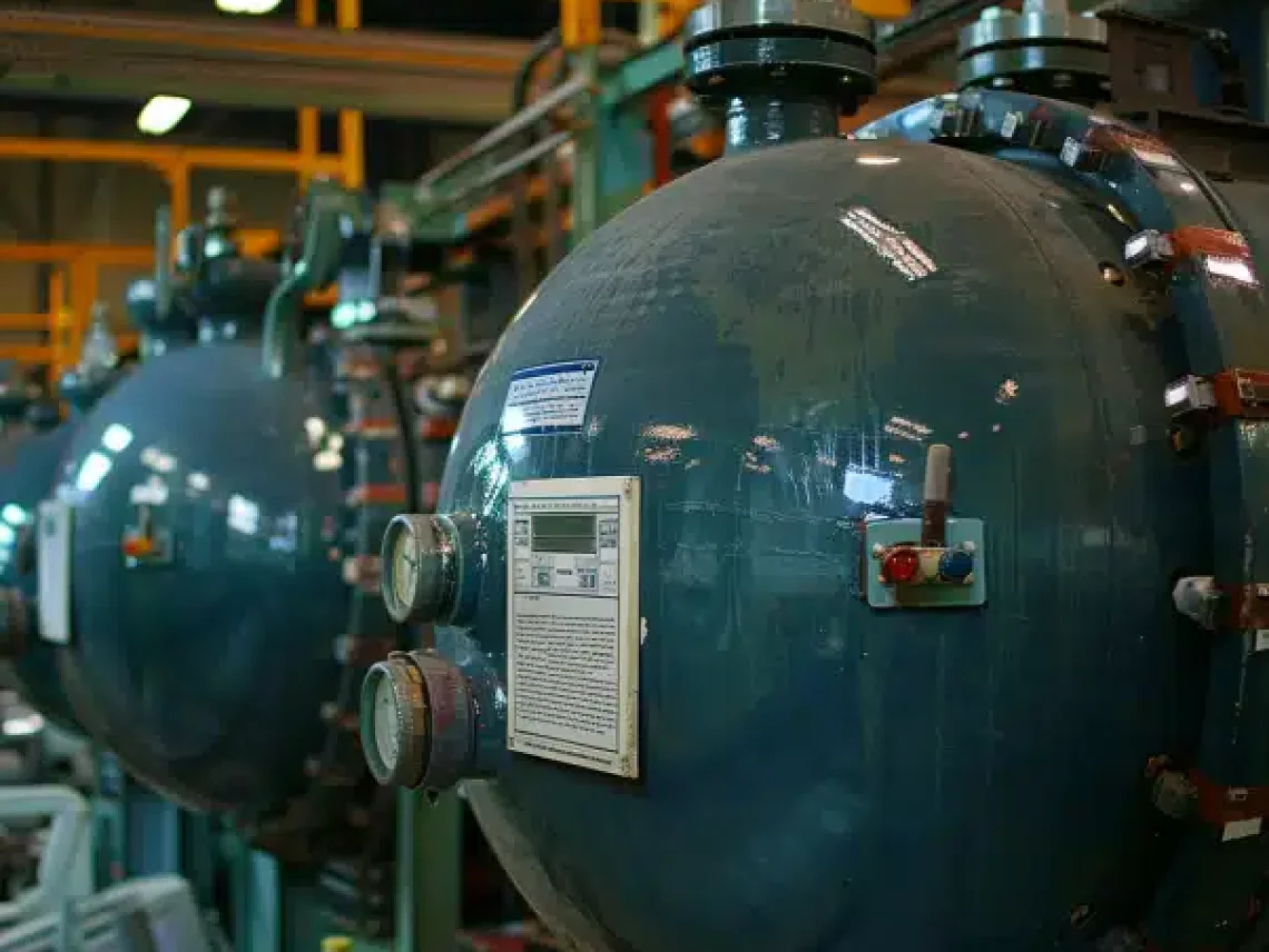 Industrial pressure vessels lined up in a manufacturing facility, equipped with gauges, control panels, and metal fittings.