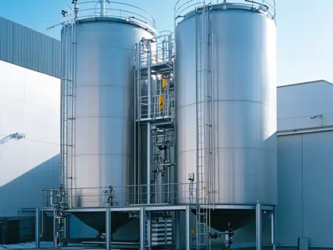 Two large metallic tanks with staircases and railings, used for industrial processes in a factory under clear skies.